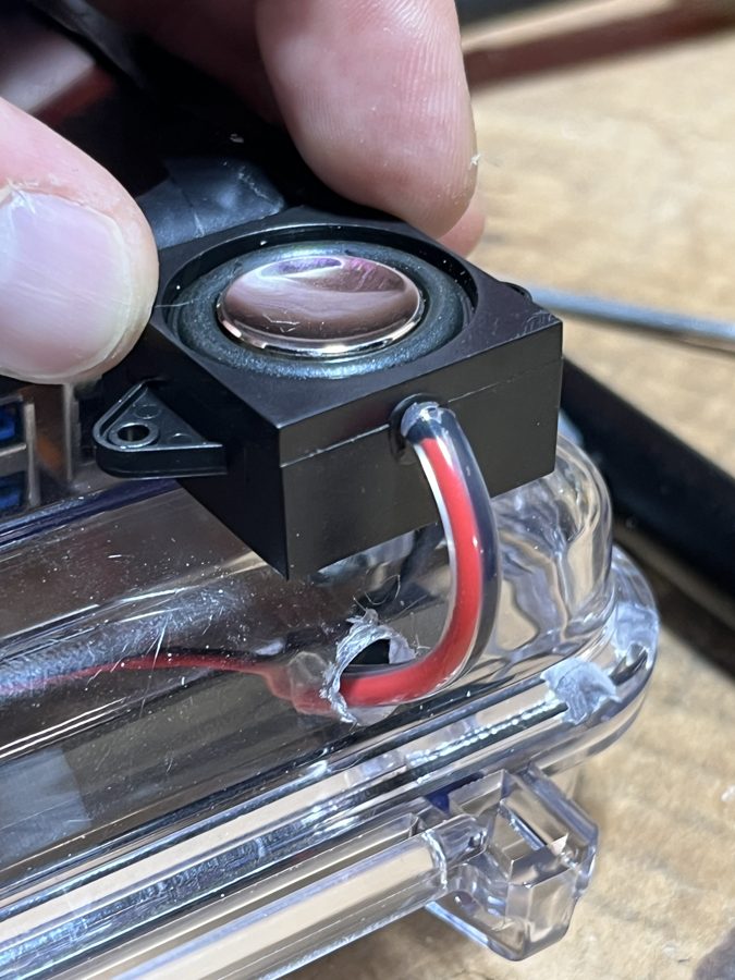 A small speaker mounted on the case with its cable sealed through the lid